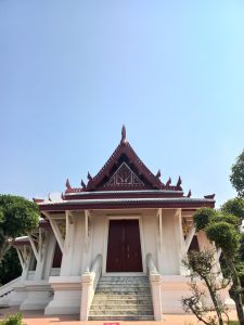 A traditional Thai temple building in Lumbini, Nepal, featuring a prominent peaked roof with intricate reddish-brown decorations.
