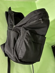 A black backpack is leaning against a green wall.