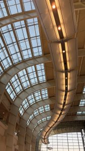 In the ceiling of a conference center, a lighting feature that curves across the full length of the ceiling.  The ceiling itself is curved and partly made of glass.