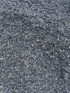 A close-up view of a textured surface made up of small, dark pebbles and gravel, showcasing various sizes and colors, predominantly shades of black, gray, and some lighter stones.