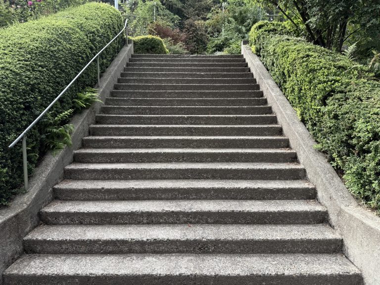 Concrete stairway framed by neatly trimmed green hedges. Leads upward into the garden area. Captured at Washington Park, Portland.