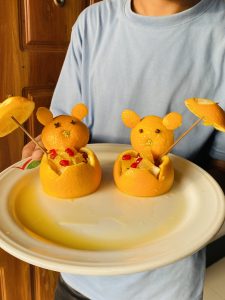 A person is holding a white plate featuring two creatively arranged orange fruit shapes resembling playful bear figures.