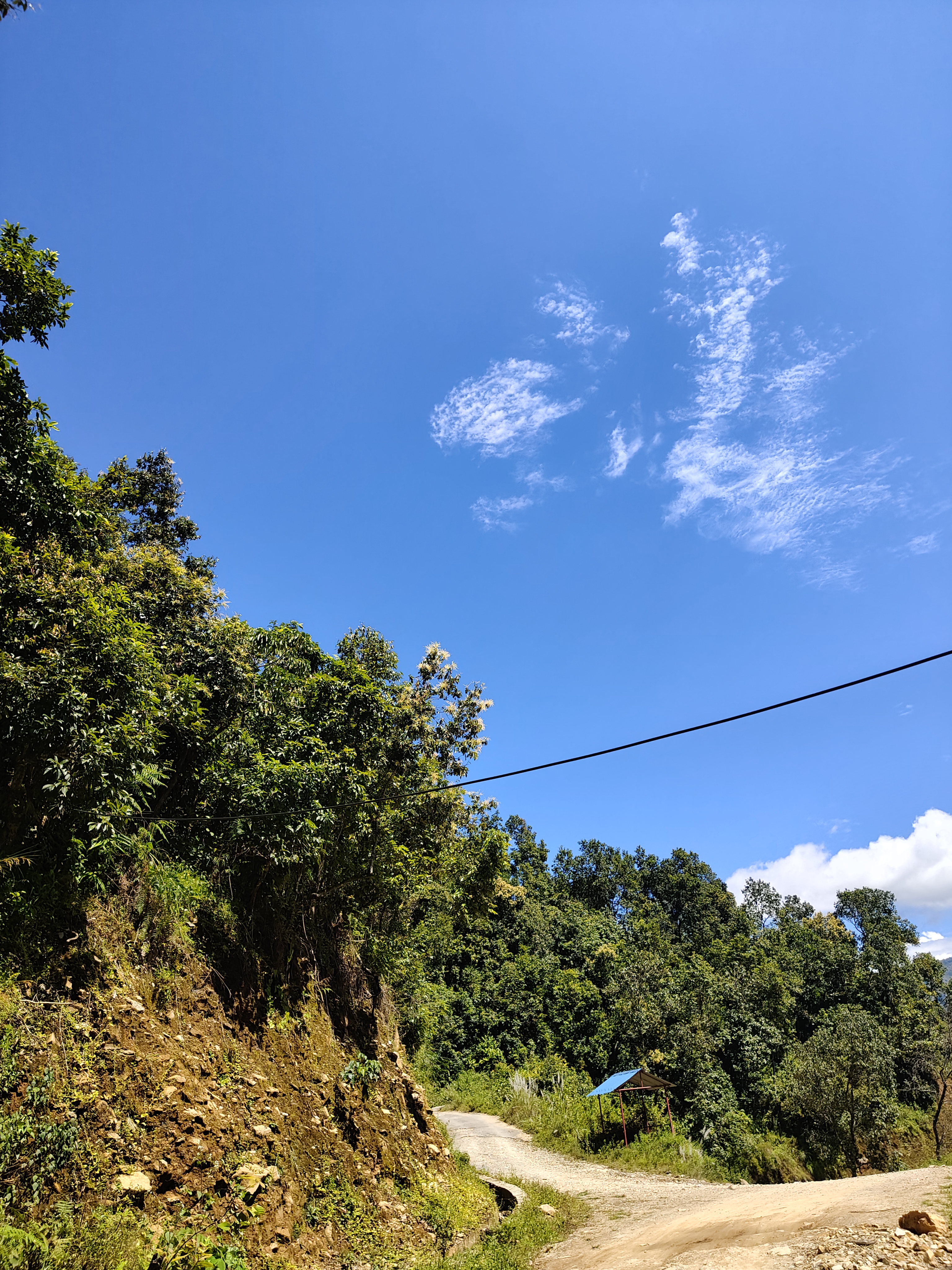 A scenic view of a clear blue sky with fluffy white clouds, overlooking a winding dirt road that leads through lush green hills