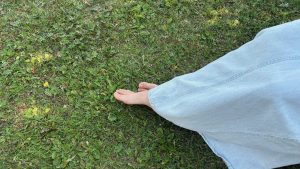 Much of the right side is filled with light blue denim, in the center some feet stick out. Most of the left side is green ground cover.