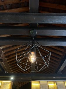 A close-up of a hanging lamp with a black metal diamond-shaped cage design, showing the bulb inside.