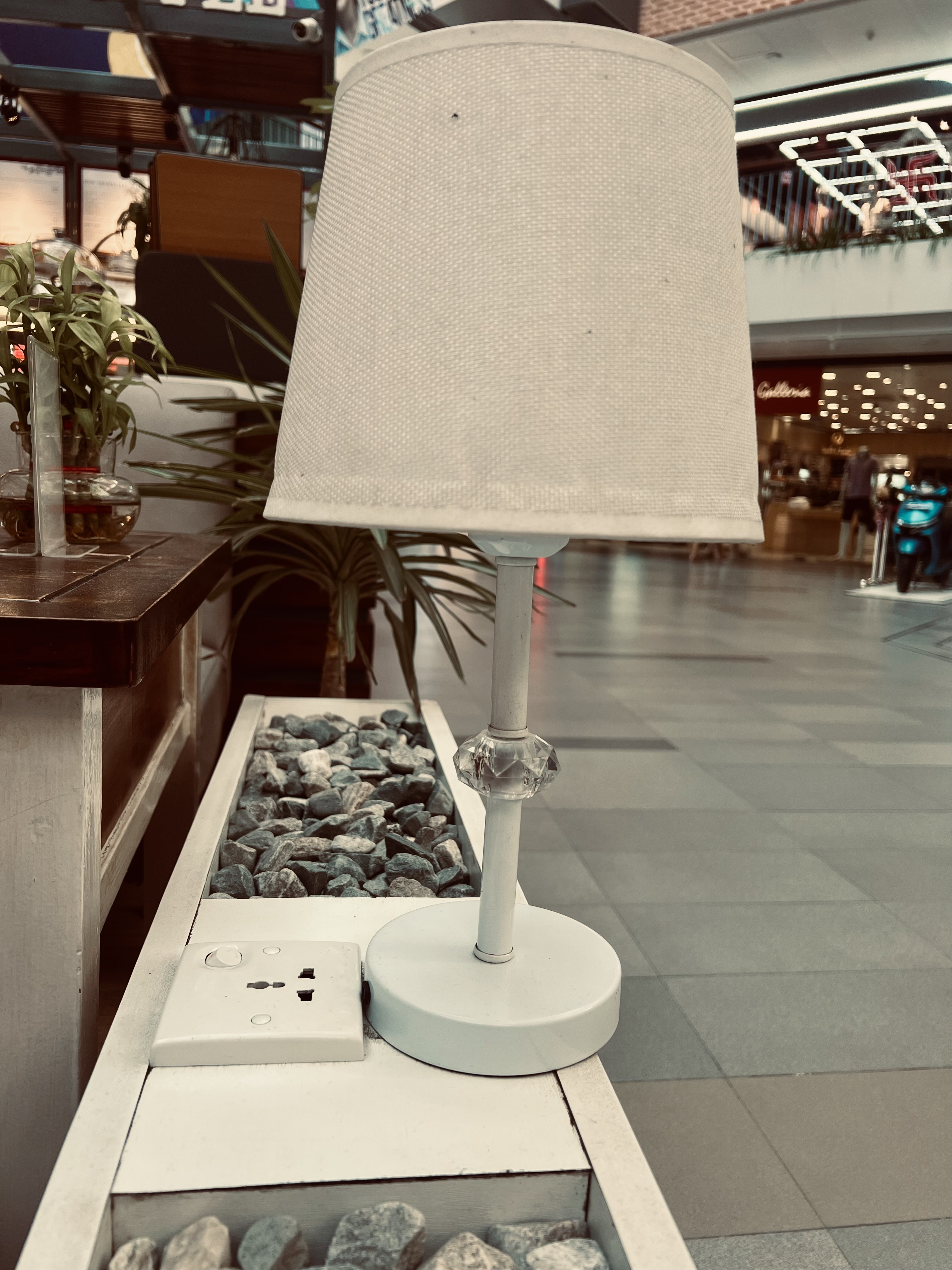 A white lampshade and its stand are pictured on a table filled with gray rocks.