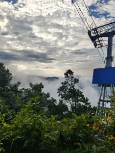 Misty mountains with lush greenery, clouds in the background, and a cable car stretching into the distance.