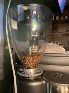A close-up view of a coffee grinder with a transparent hopper filled with coffee beans.