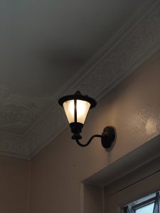 A vintage-style wall lamp with a glass shade is mounted in the corner of a room.