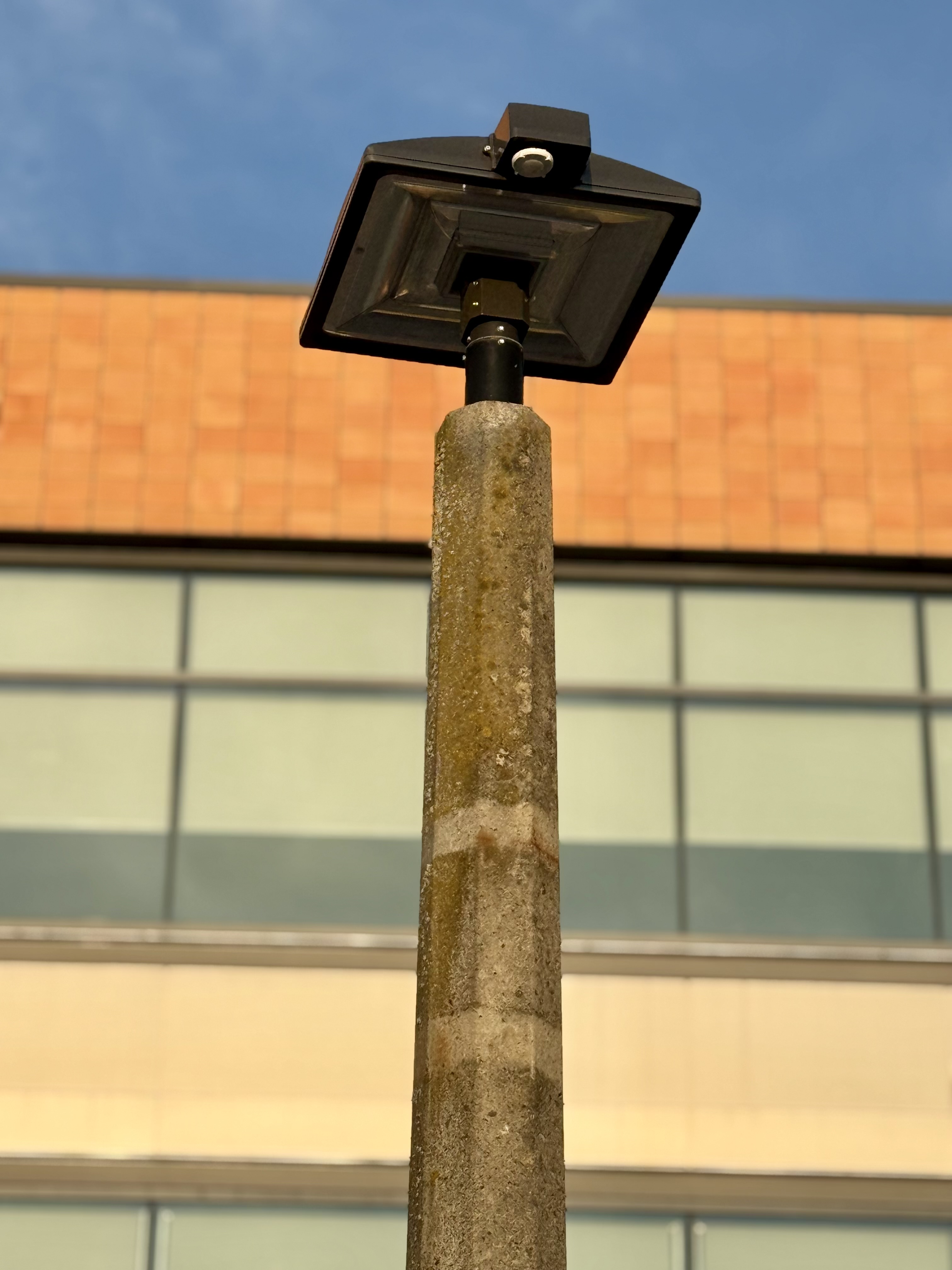 A concrete light pole with a square-shaped LED lamp captured from below, against the backdrop of a modern building. Captured from the streets of Portland. 
