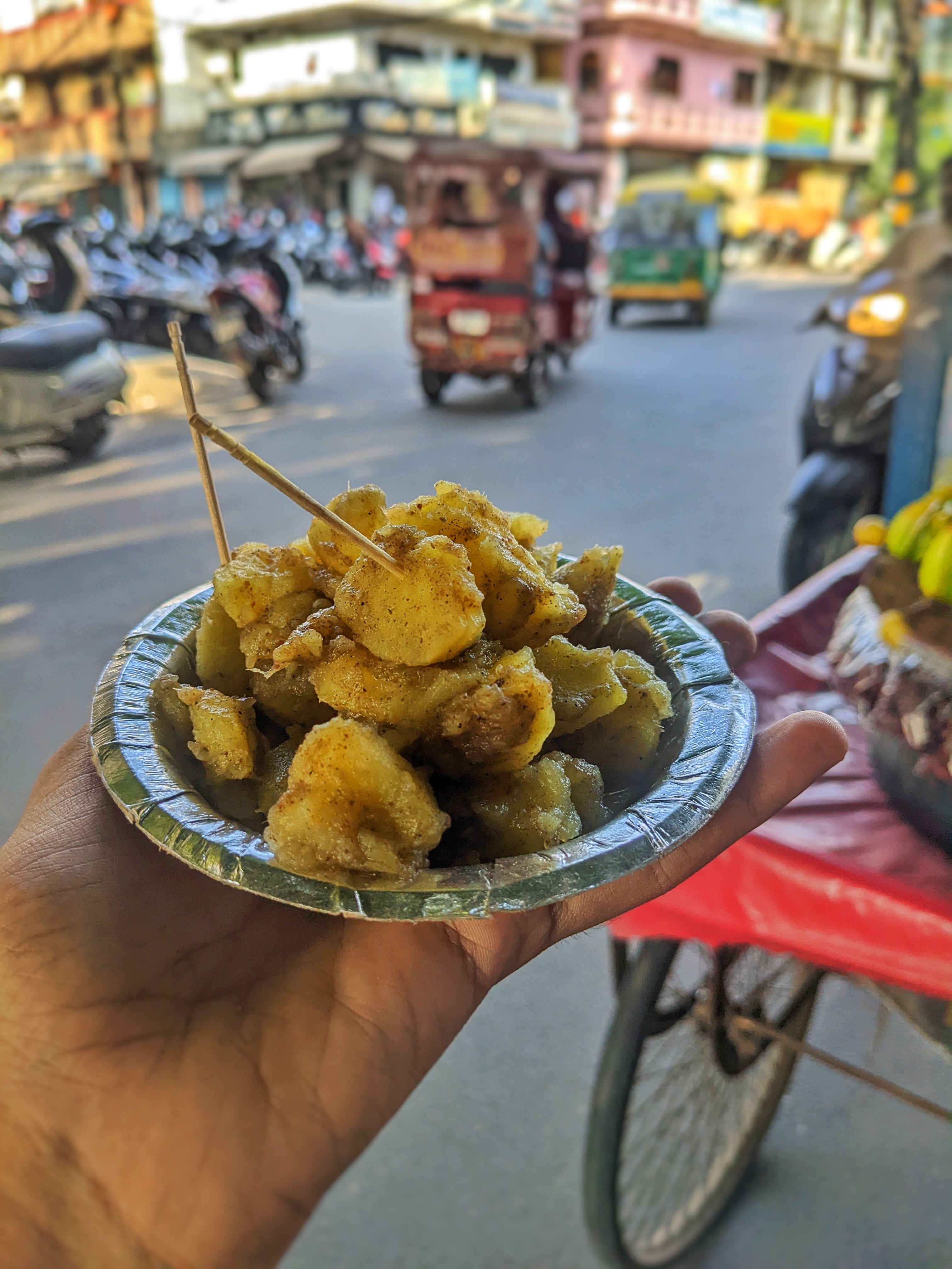 A hand holding a small, round, silver-colored plate filled with fried sweet potato snacks, lightly seasoned.