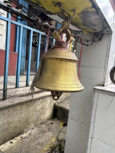 A weathered golden bell hangs from a chain, showing signs of age with some paint chipping and dirt accumulation