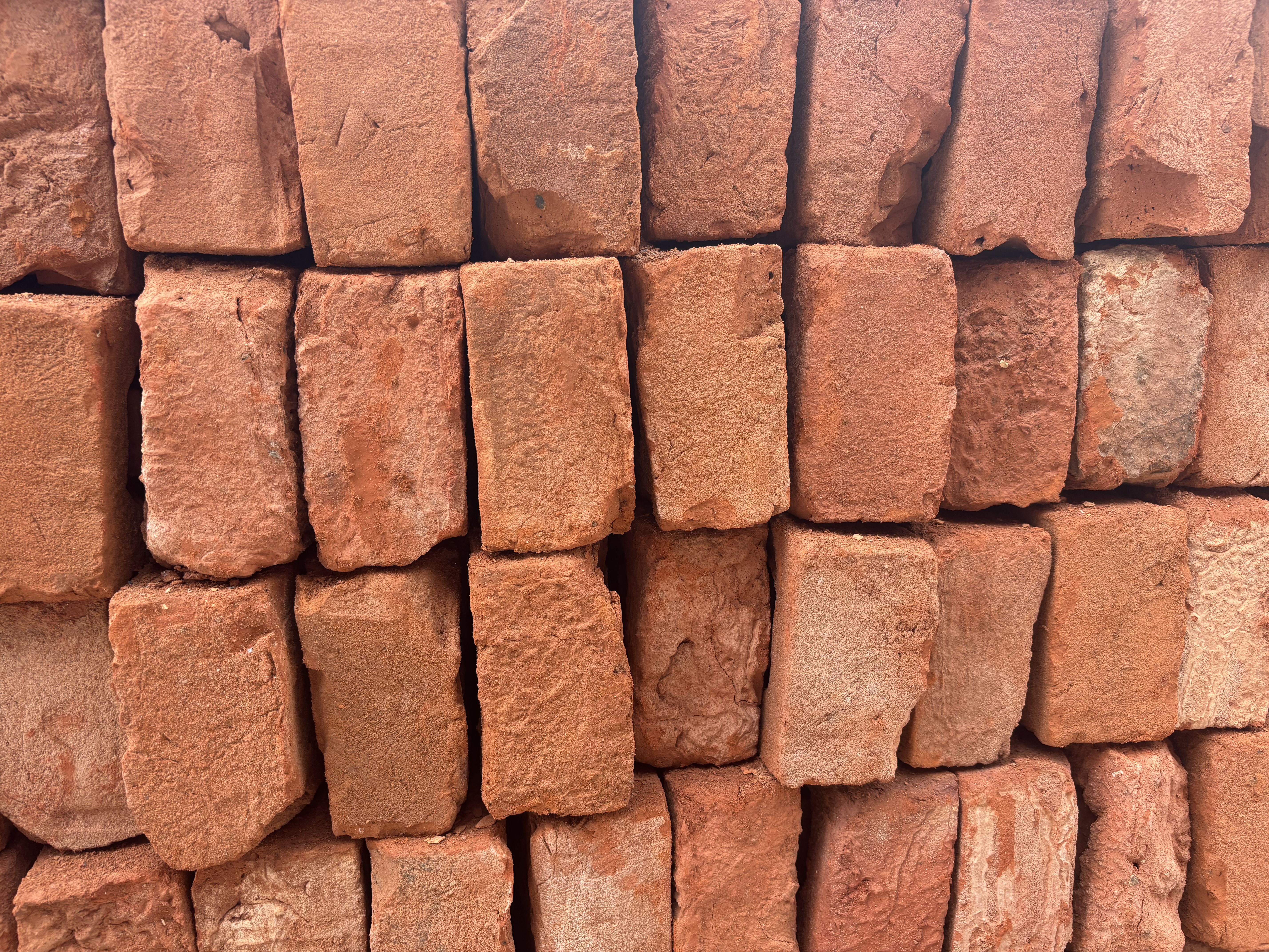 A close-up view of a stack of red bricks, showcasing the textured surfaces and various shades of orange and red.