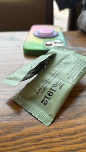 A torn open wrapper of a small condiment, close up. In the background is a cellphone, blurry.