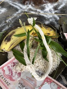 A close-up of a traditional offering arrangement featuring a ripe banana placed on a bed of uncooked white rice.