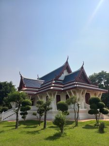 A traditional architectural structure in Lumbini, Nepal, with a multi-tiered roof featuring intricate red and blue designs, set against a clear blue sky.