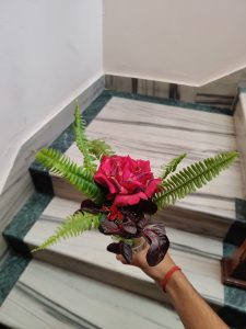 A person's hand holds a small bouquet featuring vibrant pink roses and lush green ferns.