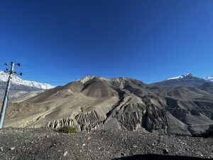 A panoramic view of a large, barren mountain range with rocky slopes and a few patches of snow on the peaks.