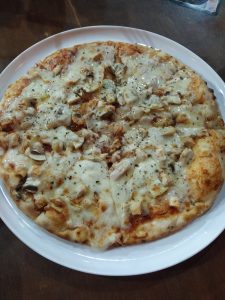 A freshly baked pizza on a white plate, topped with melted cheese, sliced mushrooms, and chunks of grilled chicken.