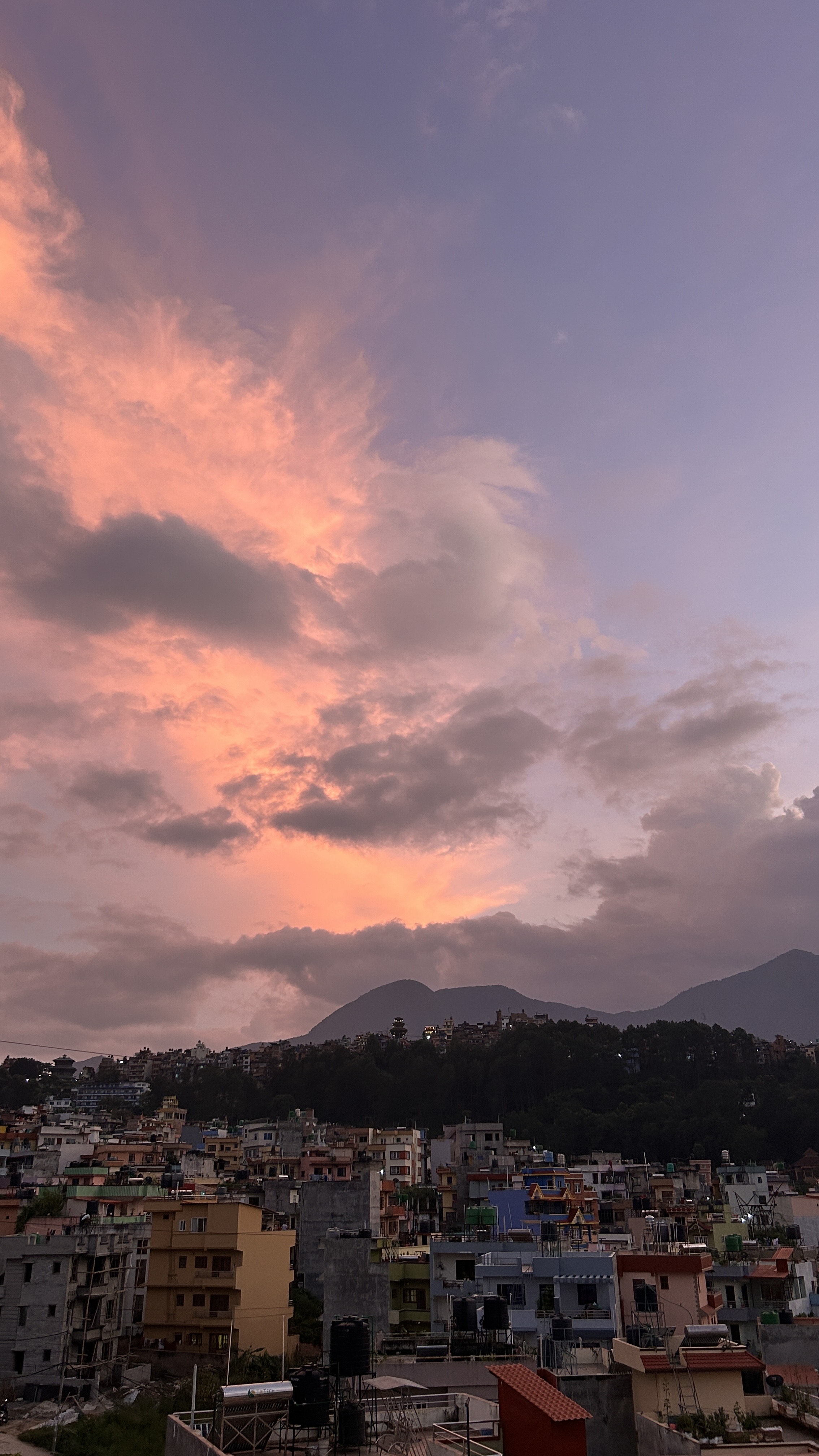 A scenic view of a city during sunset, showcasing a colorful sky filled with shades of pink and purple, dotted with soft clouds.