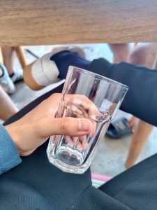 A close-up of a hand holding a clear glass with a hexagonal base, sitting on a lap.
