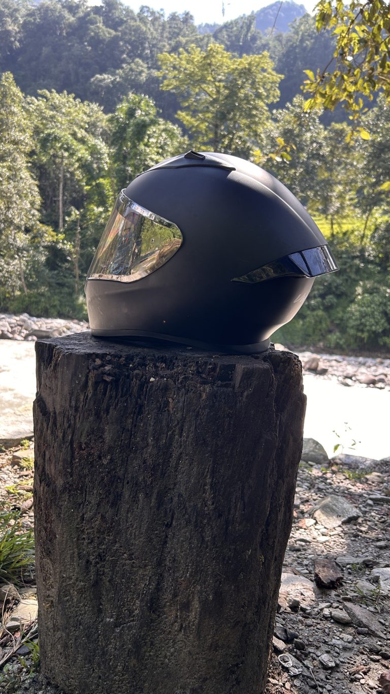 A black motorcycle helmet rests on a cut tree stump near a river.