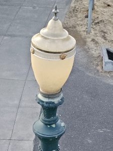 A classic-style streetlamp with peeling paint seen near Tilikum Crossing Bridge in Portland. The design has a gold and green finish.