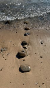A line of rocks on the beach at water&#039;s edge. They&#039;re perpendicular to the water, and descend in size as they near the water.  The larges is about the size of an adult fist.