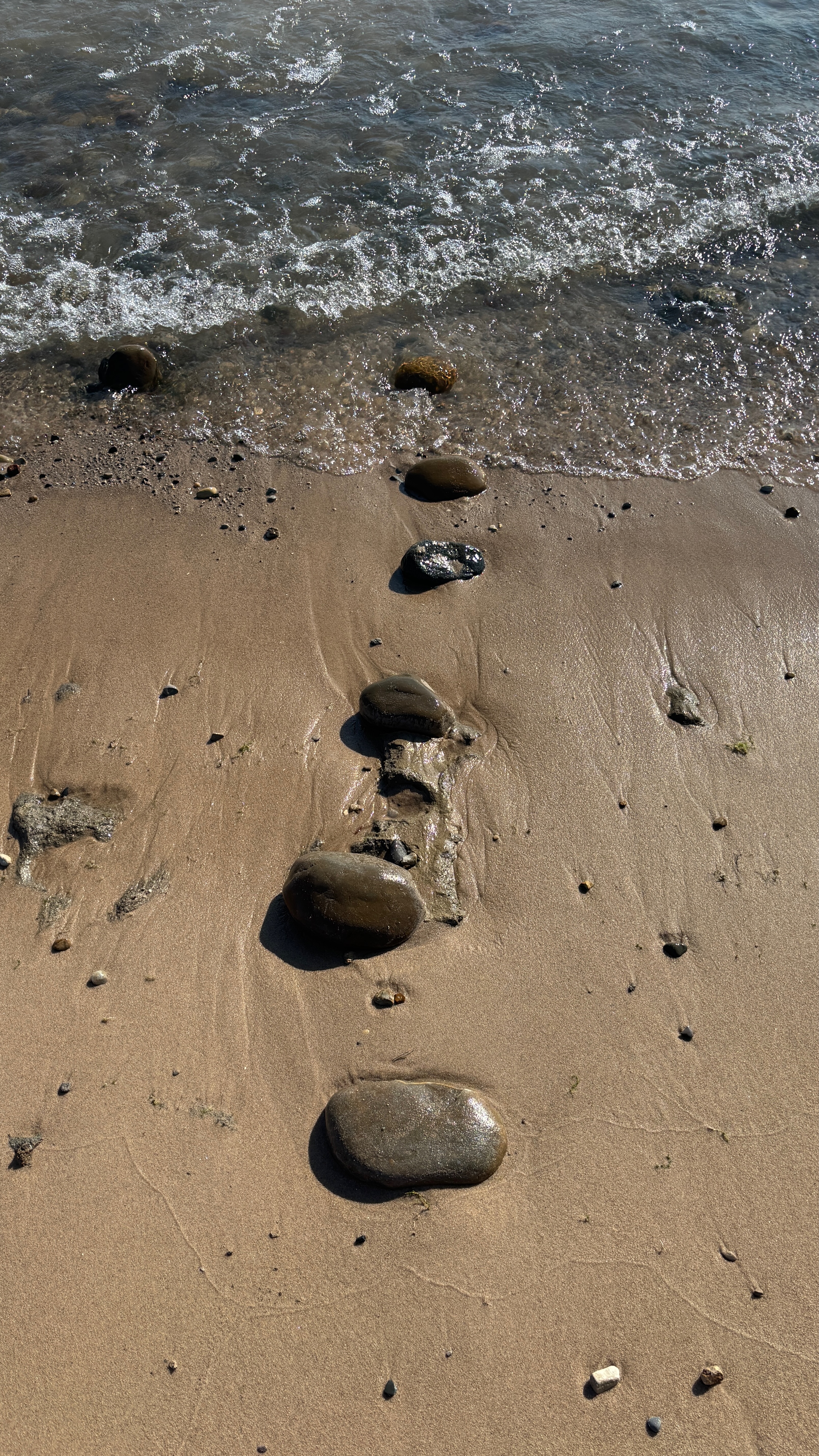 A line of rocks on the beach at water's edge. They're perpendicular to the water, and descend in size as they near the water.  The larges is about the size of an adult fist.