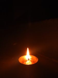 A single lit oil lamp with a bright flame, placed on a dark surface, surrounded by dim lighting.