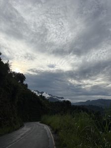 A winding road curves along a mountainous landscape under a cloudy sky. 