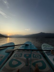 A serene sunset over a calm body of water, viewed from the perspective of three stand-up paddleboards floating in the foreground.