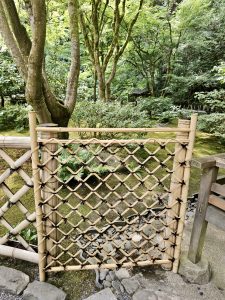 A close-up of a handcrafted bamboo gate tied with black twine, placed at the edge of a garden path in Portland Japanese Garden.