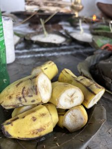 A pile of cut bananas, with some pieces displaying their yellow skin and creamy white insides, arranged on a green leaf. 