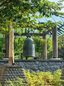 Sapporo Bell outside Portland Oregon Convention Center. It is a dark brass bell, approximately five feet tall, and it hangs in a wooden structure atop a stone dais under plexiglass. It is ornately designed.