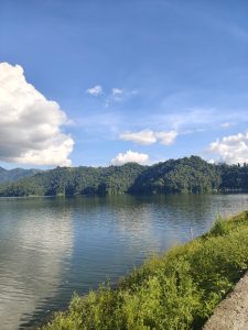 

A serene Nepal landscape with a calm lake, green hills, and a blue sky with white clouds.