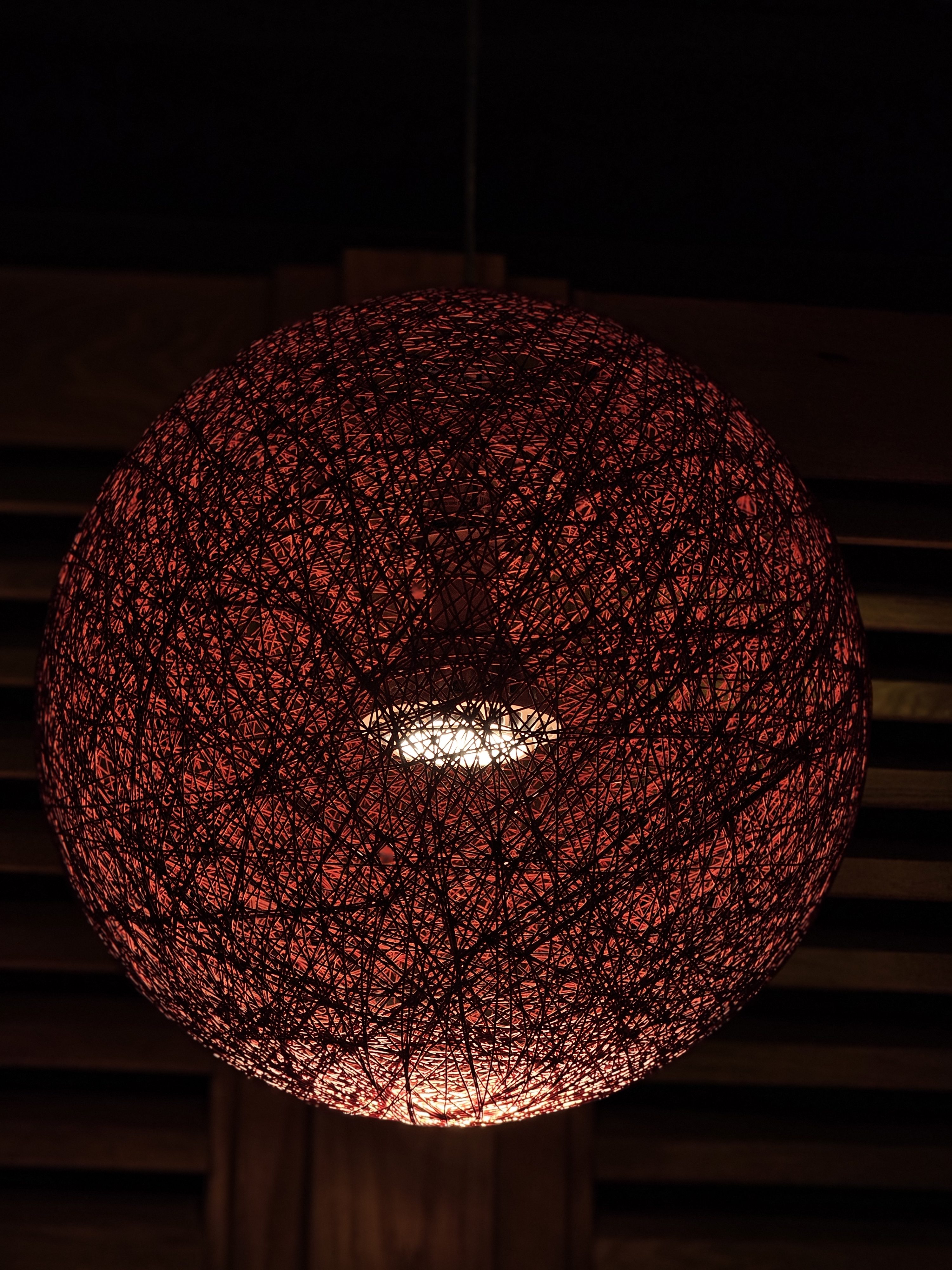 A handmade round lamp made of red threads surrounds a light bulb. The warm light glows through the threads, creating a cozy feel. Taken from downtown Portland.