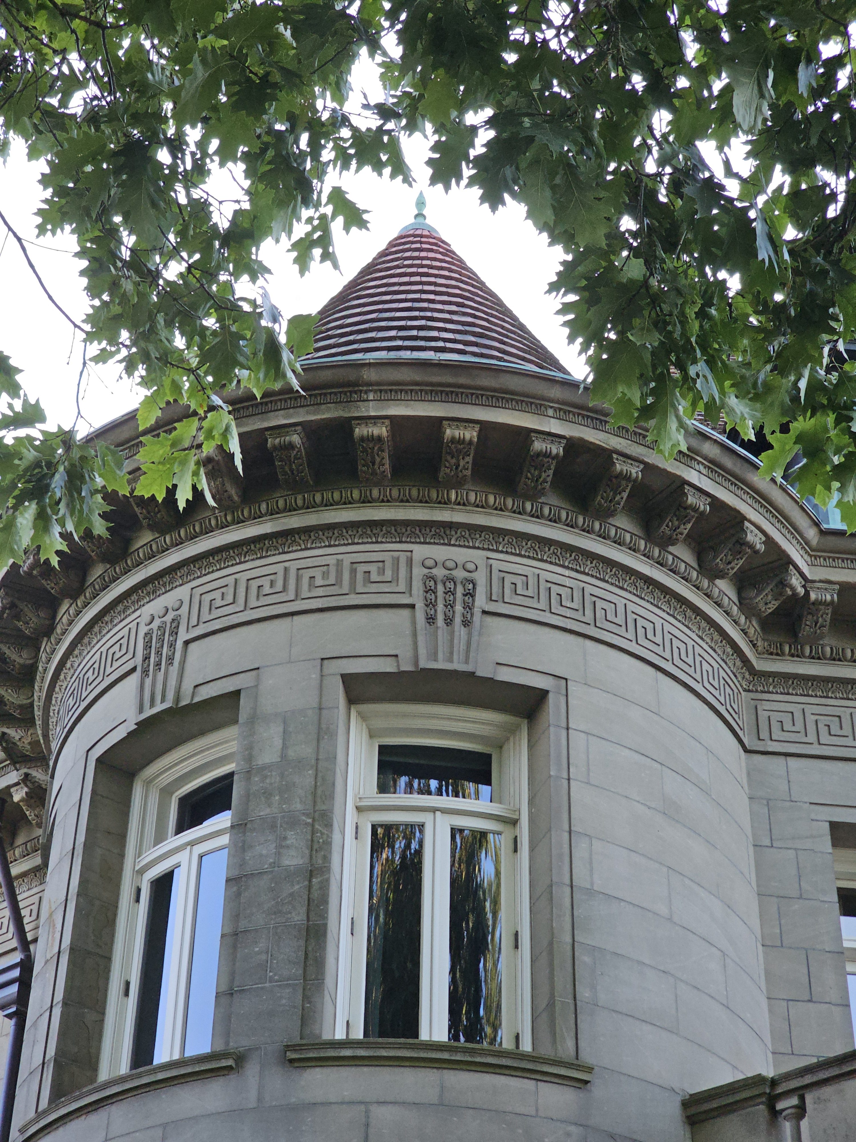 Close-up of a round turret with conical roof and stone details at Pittock Mansion, Portland. Evening sunlight highlights the elegant architecture.