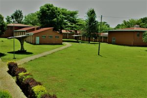 A wide view of a landscaped area featuring several buildings with orange walls and red roofs, set against a backdrop of greenery. 