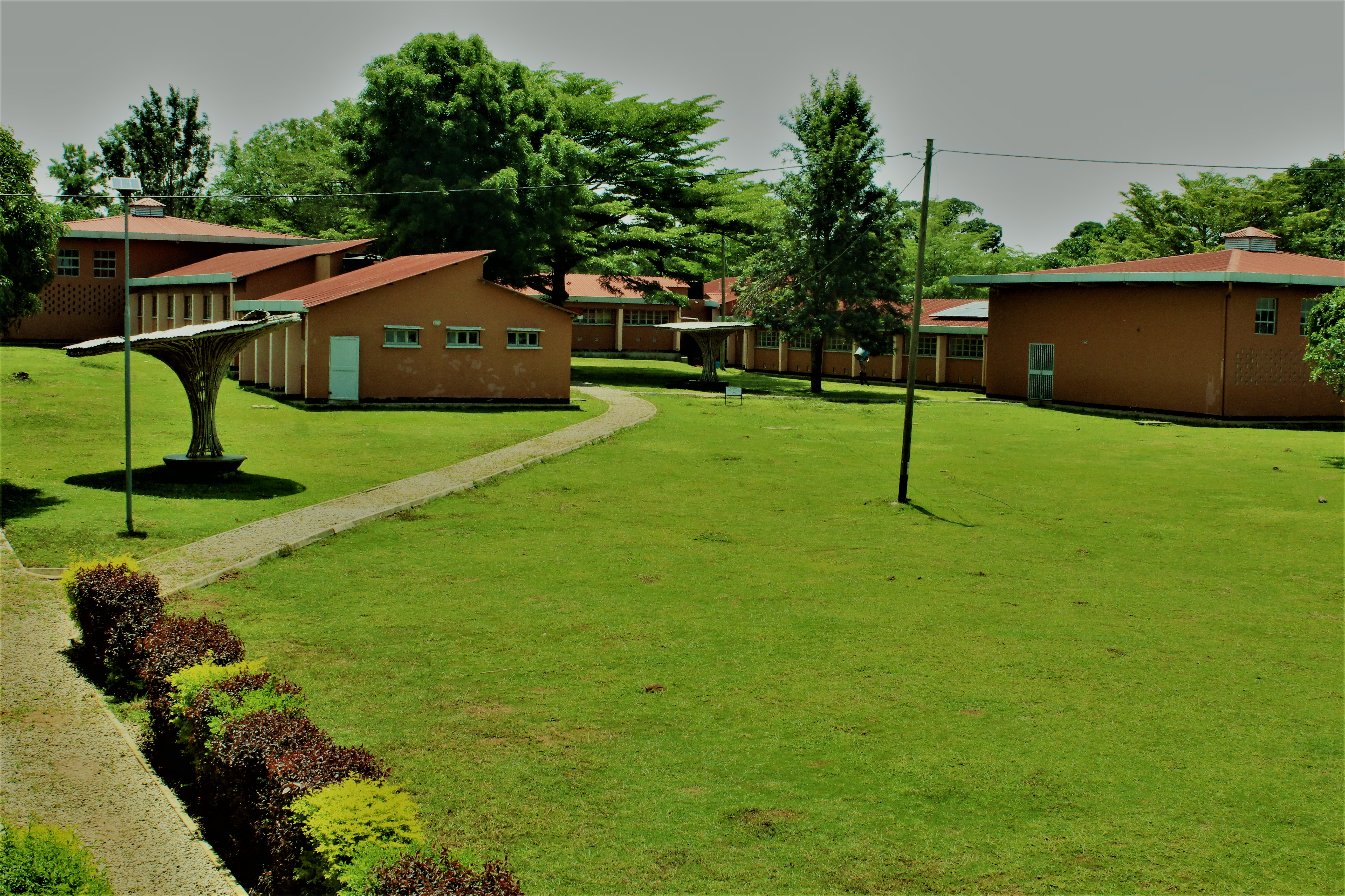 A wide view of a landscaped area featuring several buildings with orange walls and red roofs, set against a backdrop of greenery. 