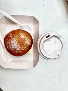 A top-down view of a powdered sugar-dusted donut in a white paper tray next to a drink with a white lid.