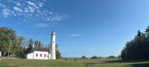 A white lighthouse with red shutters on a vast green lawn under a clear blue sky. Sturgeon Point Lighthouse, Michigan.