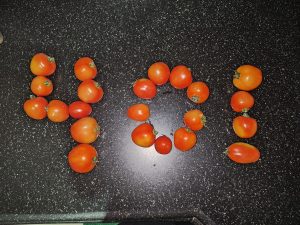 A black countertop is arranged with small, ripe red tomatoes formed into the numbers "401" and a circle. 