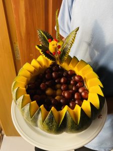 A man presents a plate with a vibrant fruit-shaped cake, showcasing intricate details.