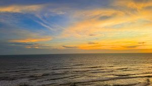 Sunset over the Bay of Bengal with gentle waves on the shore.