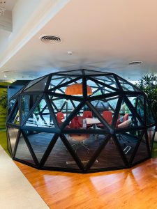 Modern glass office meeting room made with black wooden frame with red chairs and orange coloured light hung on the ceiling.