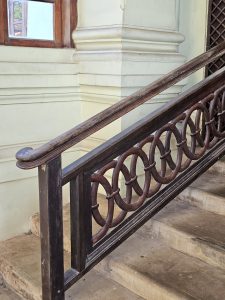 A polished wooden staircase handrail featuring repeating circular patterns. Taken inside Hill Palace, Thrippunithura, Kerala. 