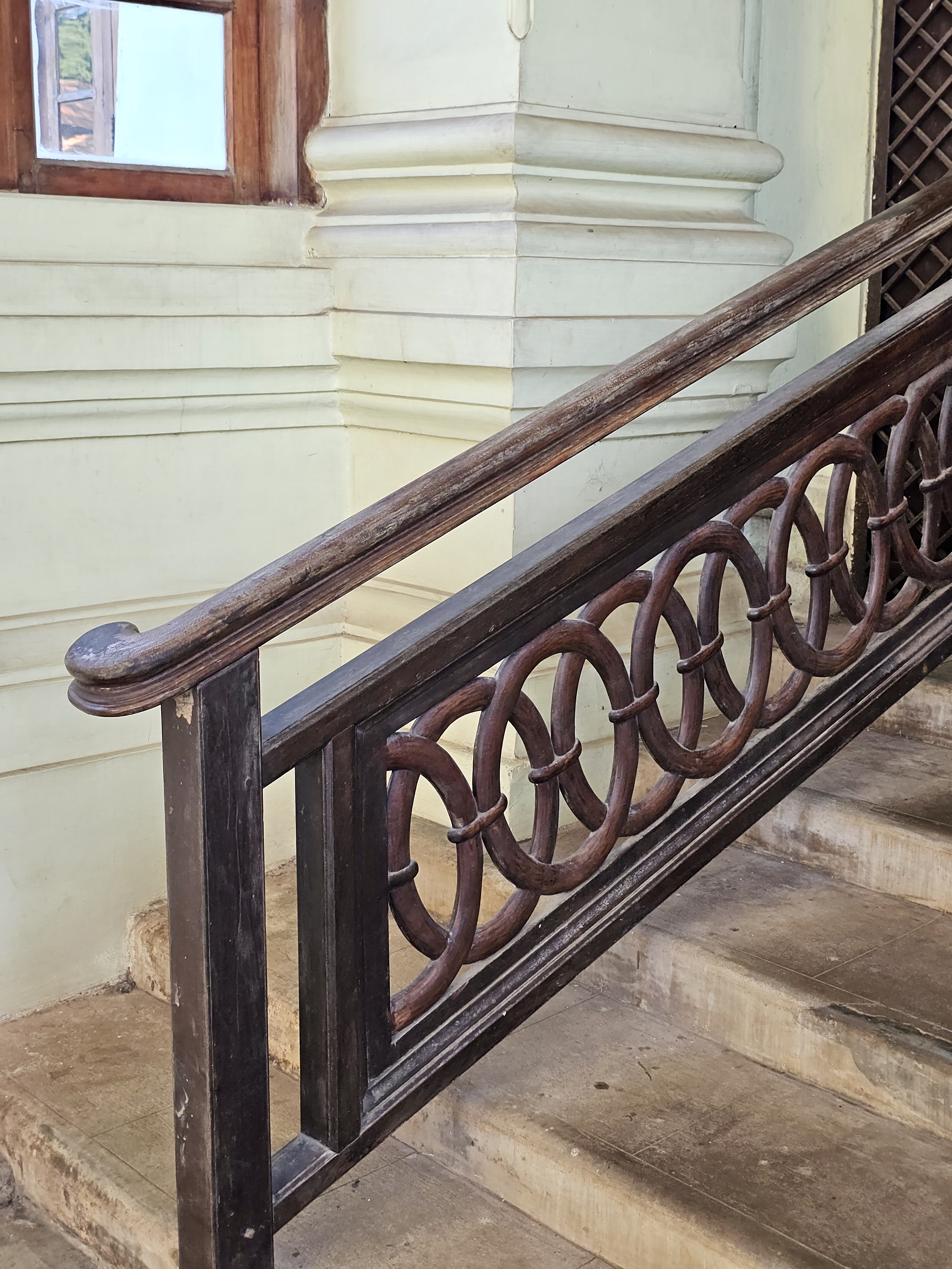A polished wooden staircase handrail featuring repeating circular patterns. Taken inside Hill Palace, Thrippunithura, Kerala. 