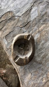 A round stone with a shallow, hollowed center sits atop a textured surface featuring layers of gray and brown hues.