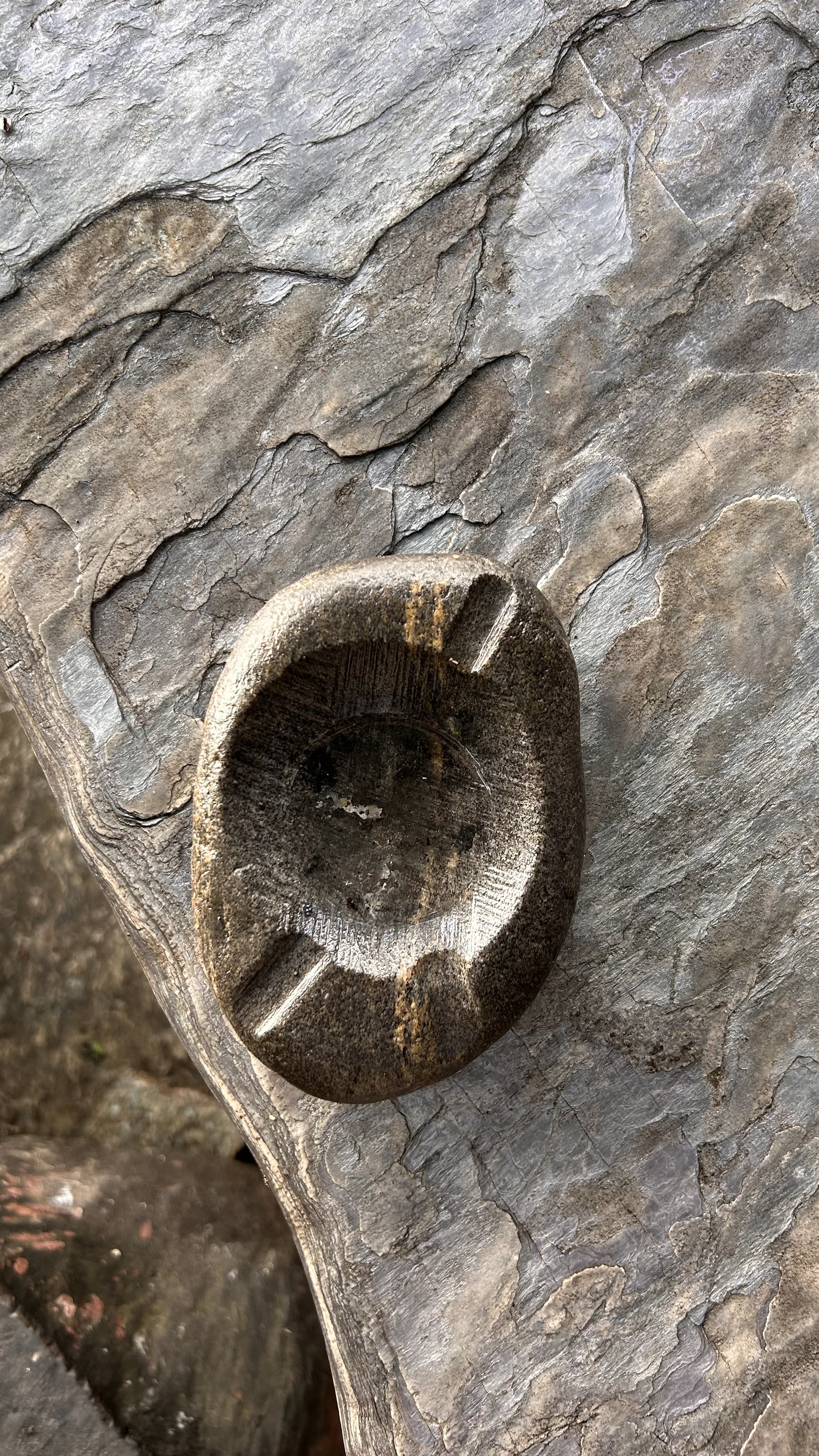 A round stone with a shallow, hollowed center sits atop a textured surface featuring layers of gray and brown hues.